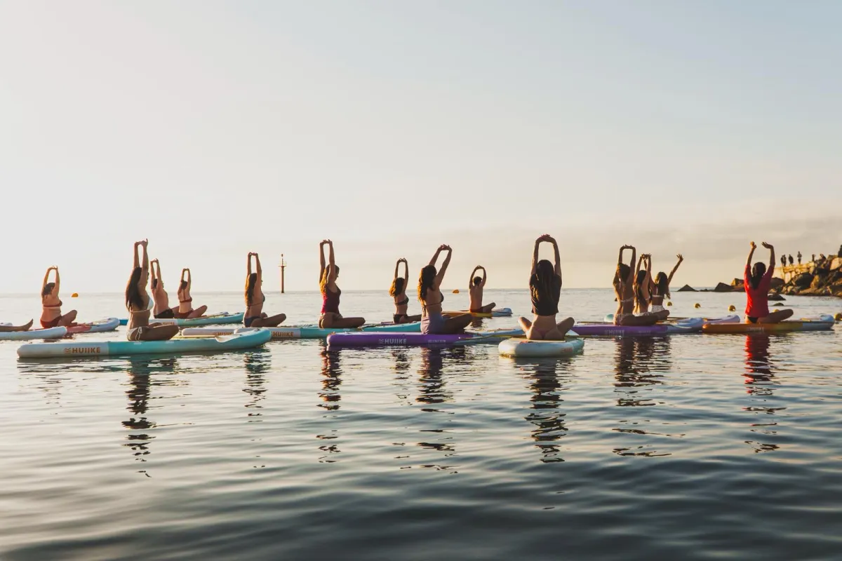 Grupo de SUP Yoga con los brazos en alto sobre las tablas en el mar en calma de Barcelona